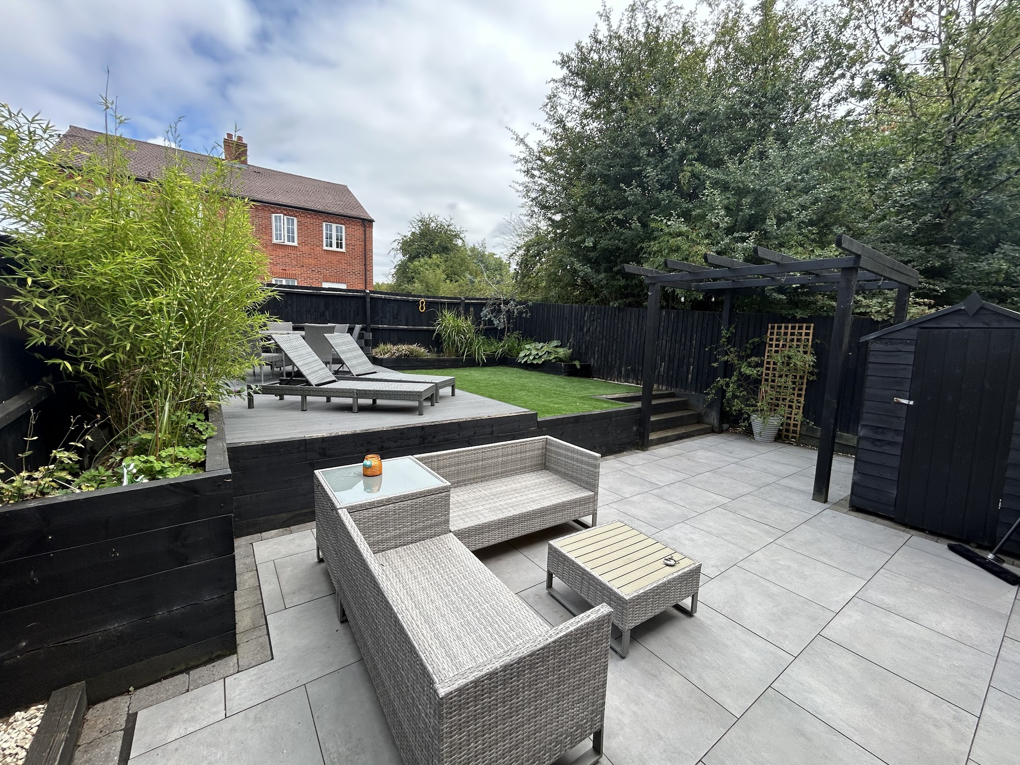 A modern grey-tiled patio with rattan furniture and raised beds